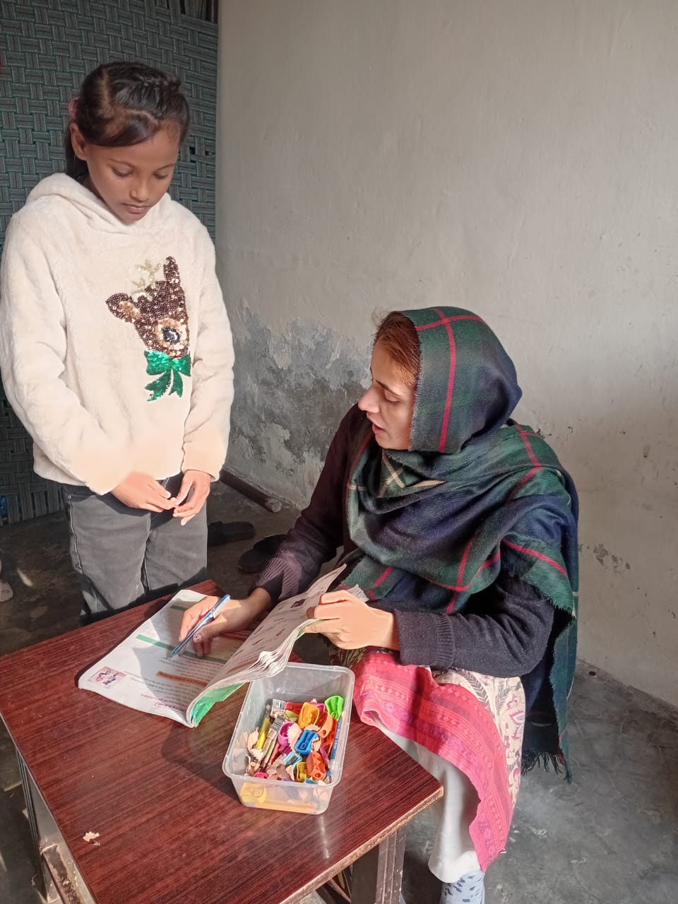 Een lerares begeleidt een meisje bij een lees- en schrijfoefening in een eenvoudig klaslokaal in Pakistan.