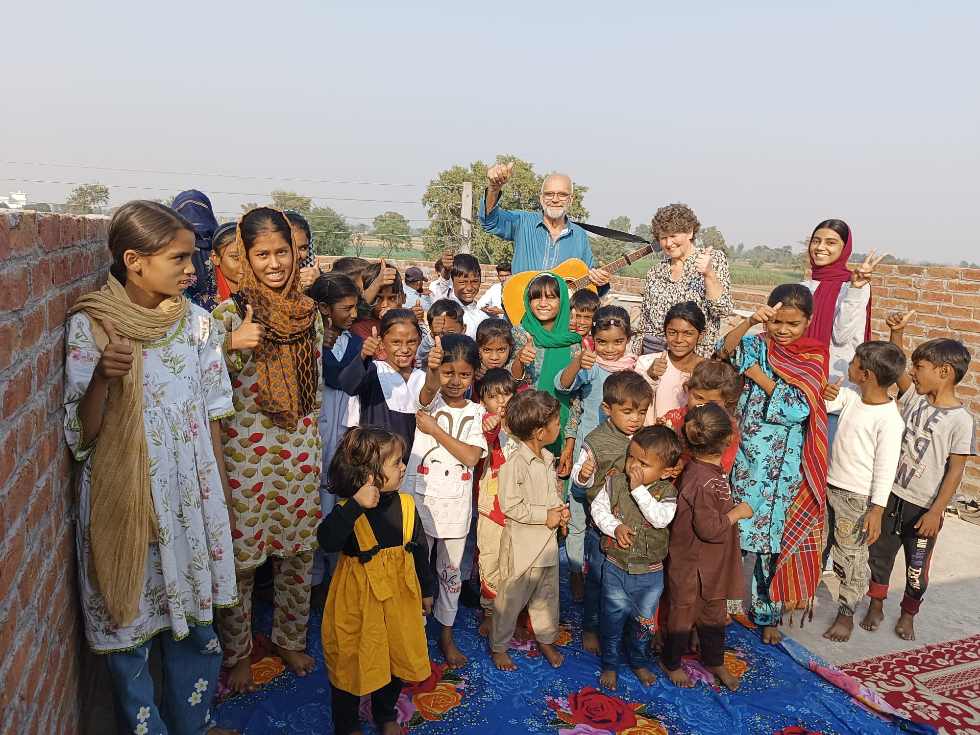 Een grote groep kinderen staat samen met Henk Muller en een medewerkster tijdens een bijeenkomst van de Pakistan Mission School.